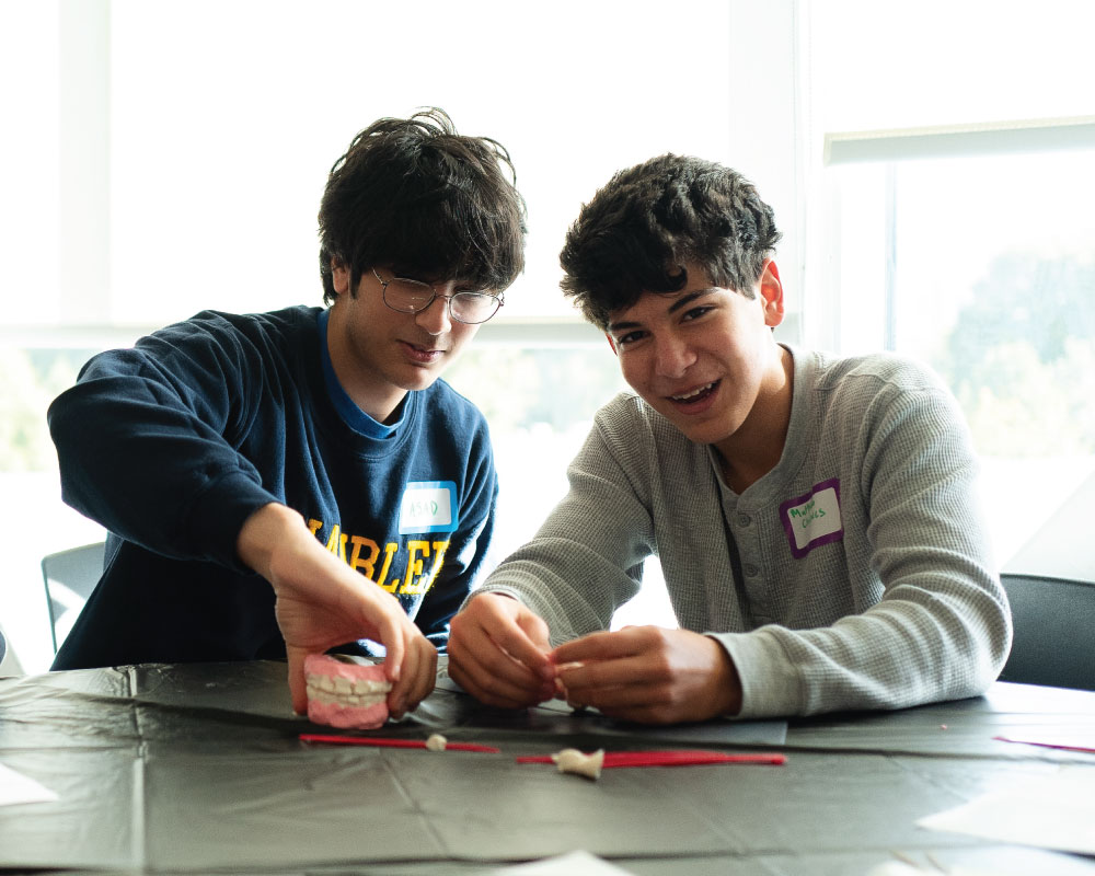 two smiling students working with a dental model