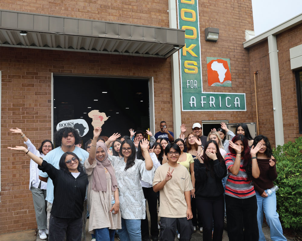 a group of students smiling and waving their hands outside a building